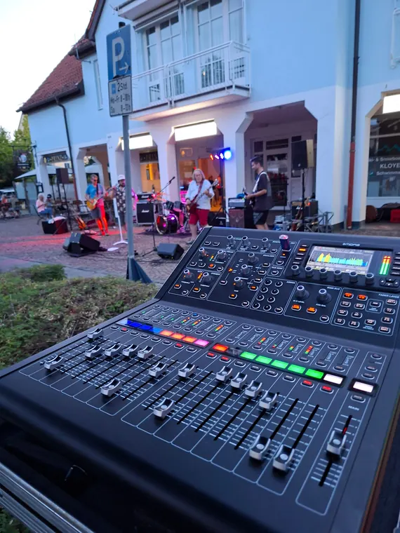 Mischpult bei Tageslicht mit Band im Hintergrund